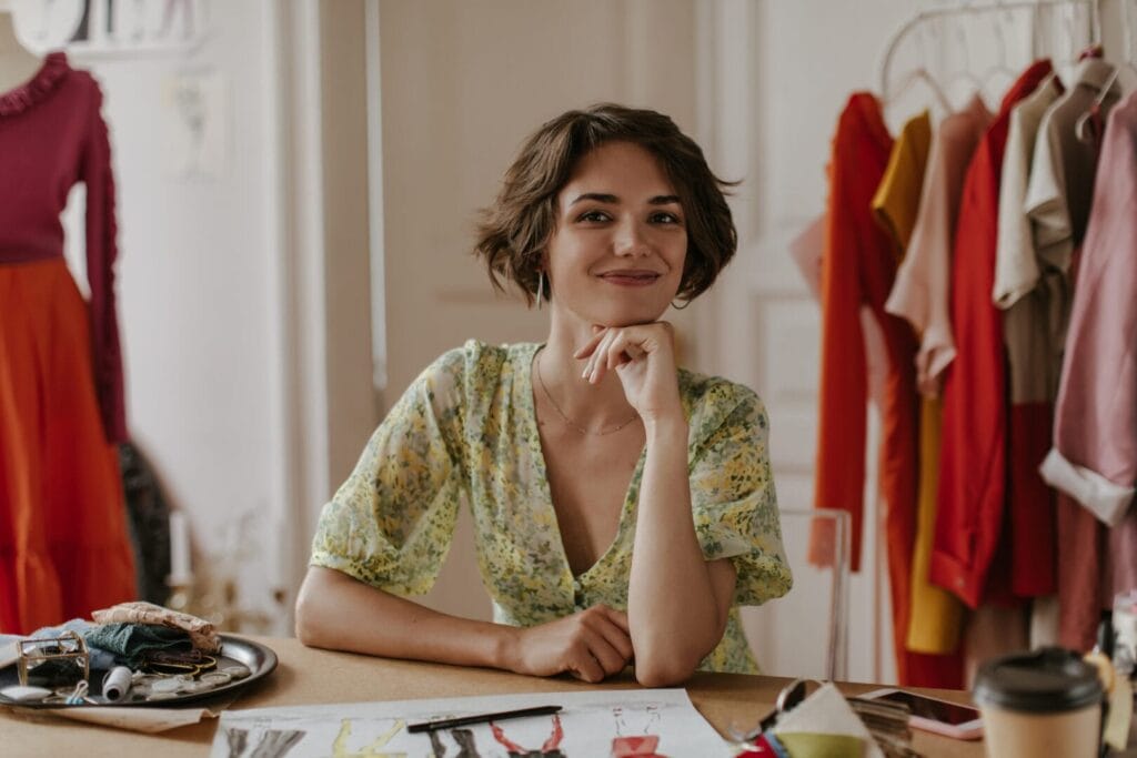 Attractive young curly short-haired woman in floral dress smiles and looks into camera. Portrait of handmade vyrobca rucnych vyrobkov vlastni eshop seo