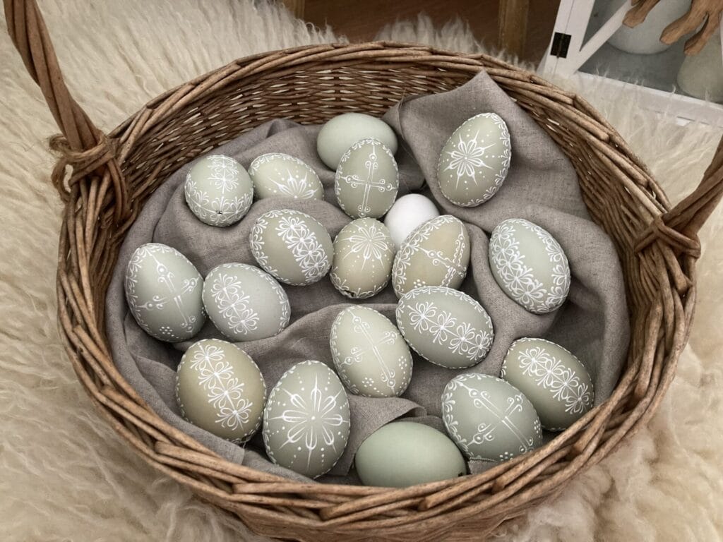 Ručne vyrobený prútený košík, sivá látka, svetlé vajcia.